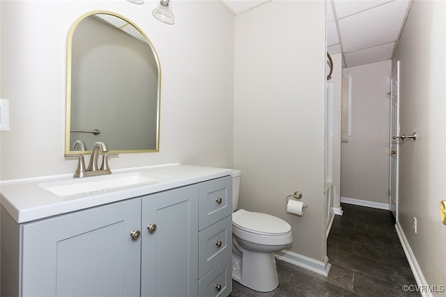 bathroom with vanity, toilet, and a drop ceiling