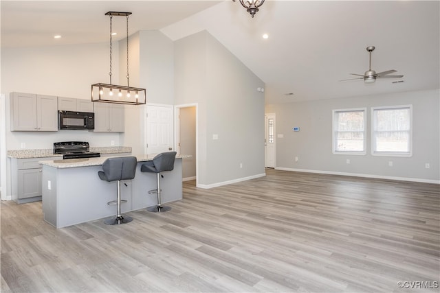 kitchen featuring light stone counters, decorative light fixtures, a kitchen island with sink, black appliances, and light wood-type flooring