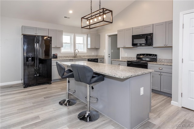 kitchen with black appliances, a kitchen island, light hardwood / wood-style flooring, and vaulted ceiling