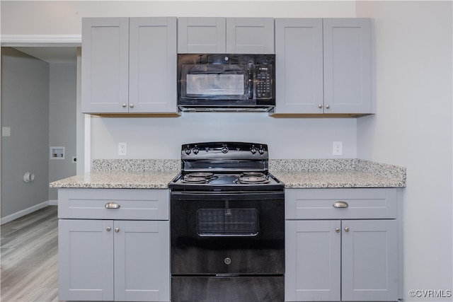 kitchen with gray cabinets, light stone counters, light hardwood / wood-style flooring, and black appliances