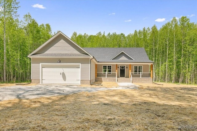 ranch-style house with covered porch, an attached garage, a forest view, and gravel driveway
