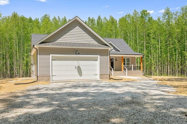 view of front of property featuring driveway, a view of trees, covered porch, an attached garage, and a shingled roof