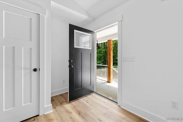 foyer entrance featuring light wood-type flooring, vaulted ceiling, and baseboards