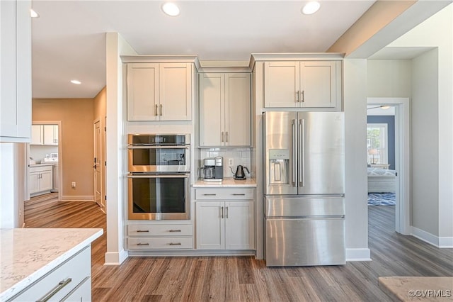 kitchen with decorative backsplash, light stone countertops, hardwood / wood-style floors, and appliances with stainless steel finishes