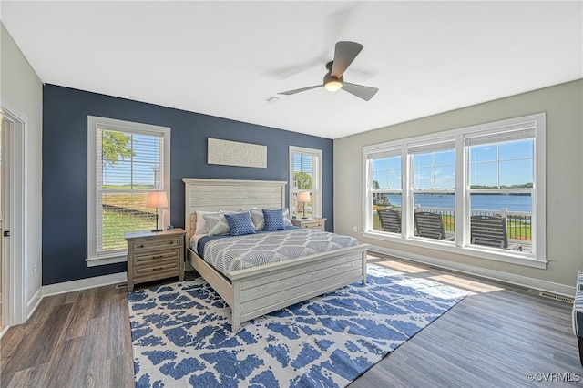 bedroom with multiple windows, ceiling fan, a water view, and dark hardwood / wood-style floors