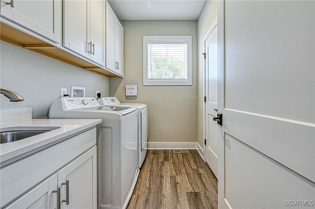 clothes washing area with hardwood / wood-style floors, washer and dryer, cabinets, and sink