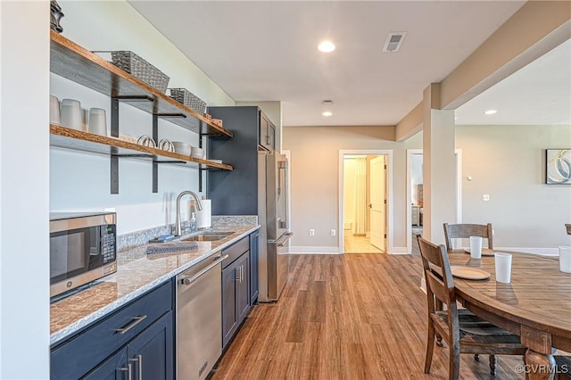 kitchen featuring sink, blue cabinetry, light hardwood / wood-style floors, light stone counters, and stainless steel appliances