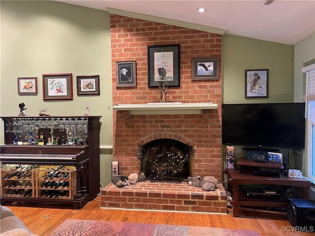 living room with a brick fireplace, wood-type flooring, and vaulted ceiling