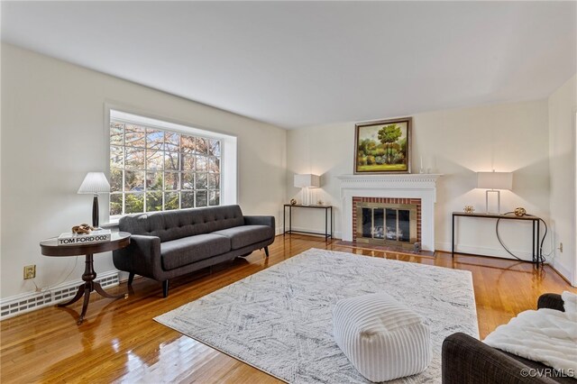 living room featuring hardwood / wood-style floors, a baseboard heating unit, and a brick fireplace