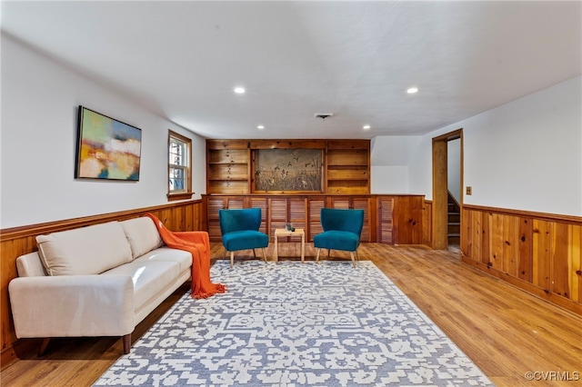 living room featuring built in shelves, wood walls, and light wood-type flooring