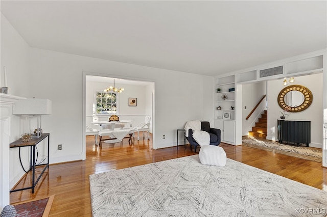 living area with wood-type flooring, an inviting chandelier, and built in shelves