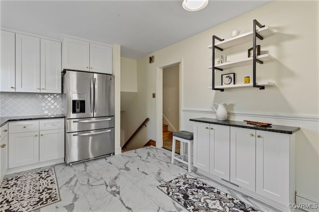 kitchen featuring white cabinets, stainless steel refrigerator with ice dispenser, backsplash, and dark stone countertops