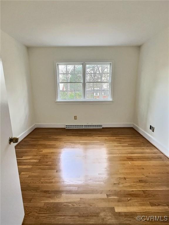 empty room with hardwood / wood-style flooring and a baseboard heating unit