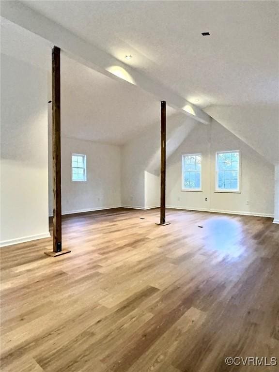 additional living space featuring vaulted ceiling with beams, hardwood / wood-style flooring, and a healthy amount of sunlight