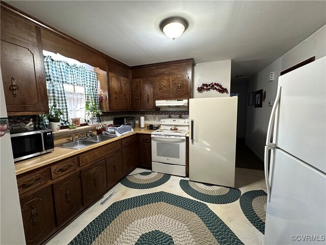 kitchen with dark brown cabinetry, sink, light tile patterned floors, white appliances, and decorative backsplash