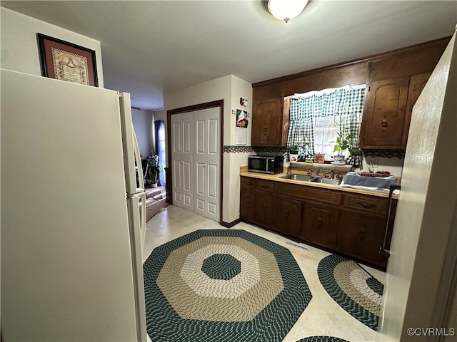 kitchen with dark brown cabinetry, sink, backsplash, and white fridge