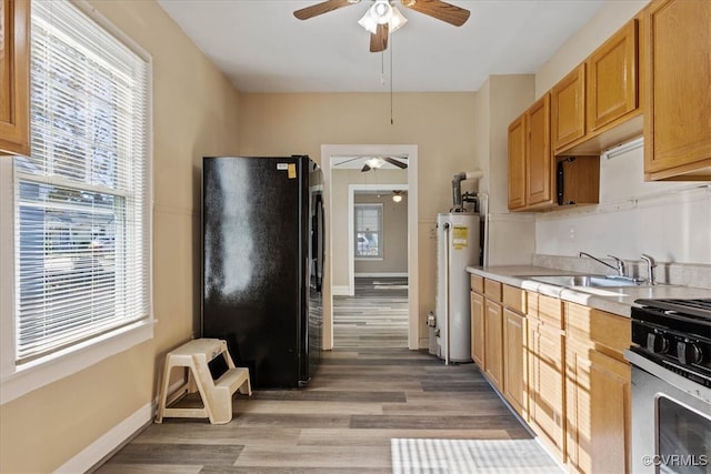 kitchen featuring stainless steel gas range oven, black refrigerator, gas water heater, sink, and light hardwood / wood-style flooring