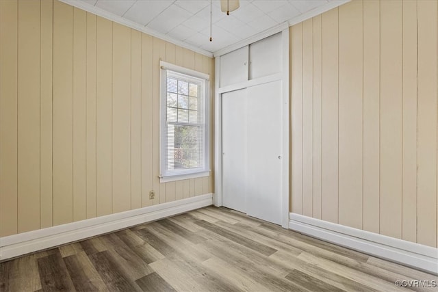 unfurnished bedroom with ceiling fan, crown molding, light hardwood / wood-style flooring, a closet, and wood walls