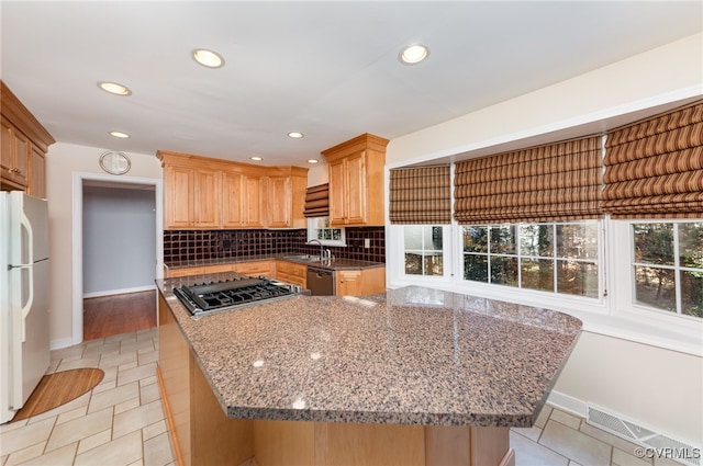 kitchen with sink, light tile patterned floors, appliances with stainless steel finishes, dark stone counters, and decorative backsplash