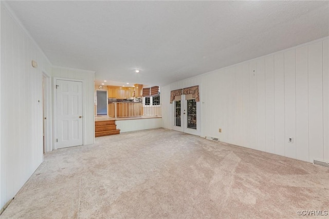 unfurnished living room with wooden walls, light colored carpet, and french doors