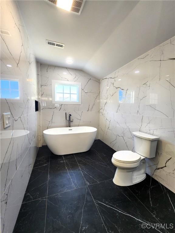 bathroom with vaulted ceiling, a tub, tile walls, and toilet