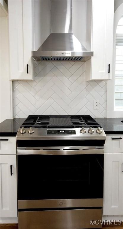 kitchen with tasteful backsplash, stainless steel range oven, white cabinets, and wall chimney range hood