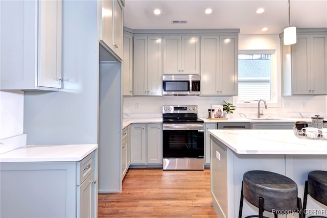 kitchen featuring a kitchen bar, light wood-type flooring, stainless steel appliances, sink, and pendant lighting