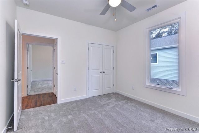 unfurnished bedroom with dark colored carpet, a closet, and ceiling fan