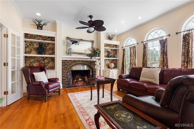 living room featuring hardwood / wood-style floors, ceiling fan, a fireplace, and crown molding