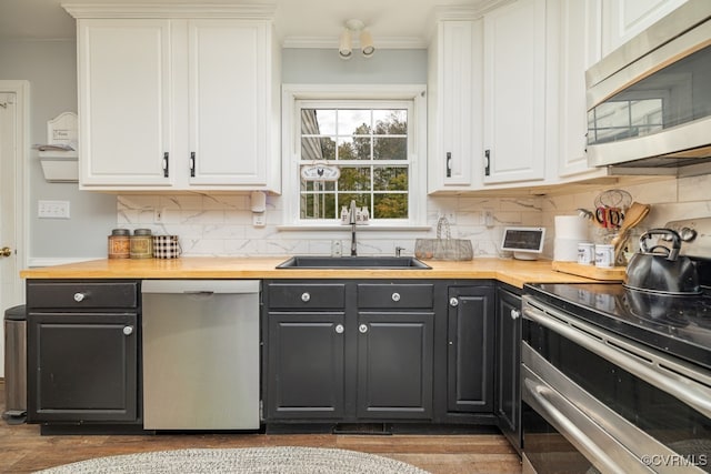 kitchen with stainless steel appliances, sink, backsplash, white cabinets, and butcher block countertops