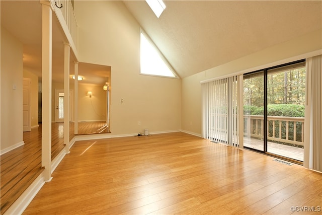 spare room featuring high vaulted ceiling, light hardwood / wood-style floors, and a skylight