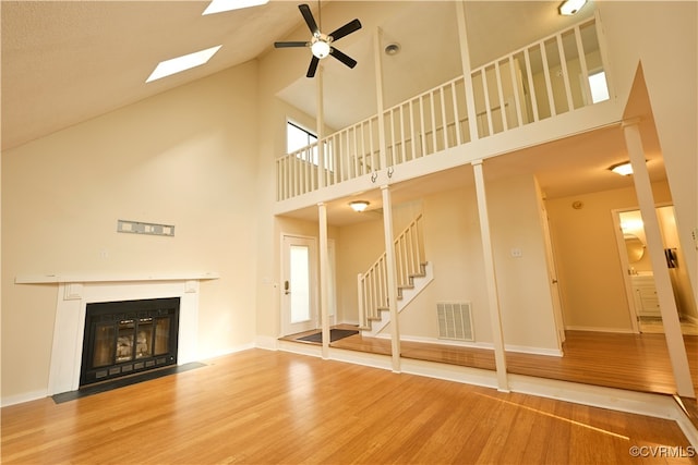 unfurnished living room featuring ceiling fan, wood-type flooring, a skylight, and high vaulted ceiling