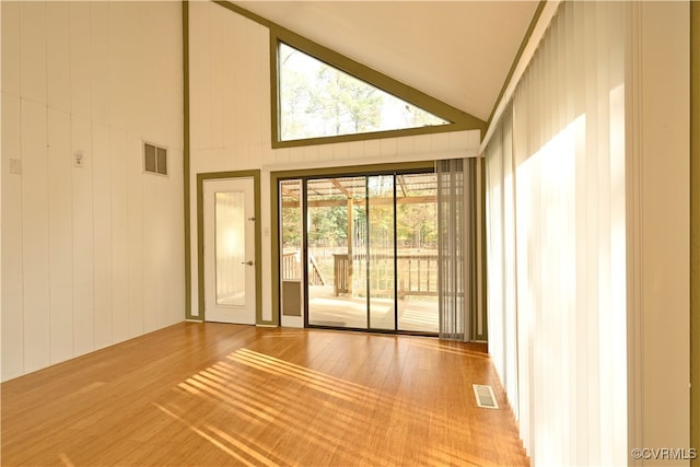 empty room with high vaulted ceiling, wooden walls, and hardwood / wood-style flooring