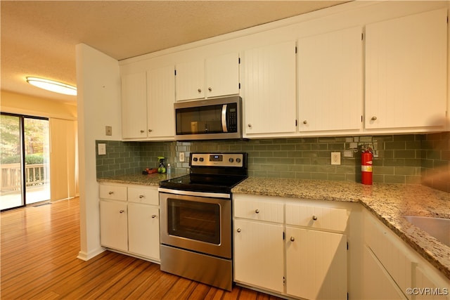 kitchen featuring tasteful backsplash, stainless steel appliances, light wood-type flooring, white cabinetry, and a textured ceiling