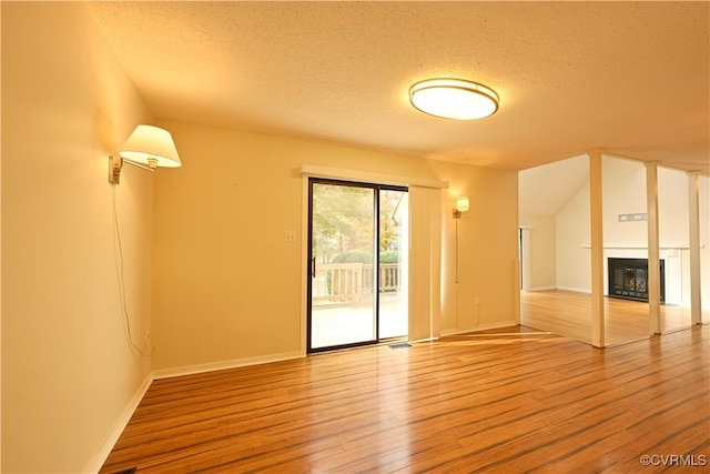 unfurnished living room with hardwood / wood-style flooring, a textured ceiling, and vaulted ceiling