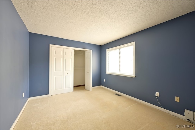 unfurnished bedroom with a closet, a textured ceiling, and light carpet