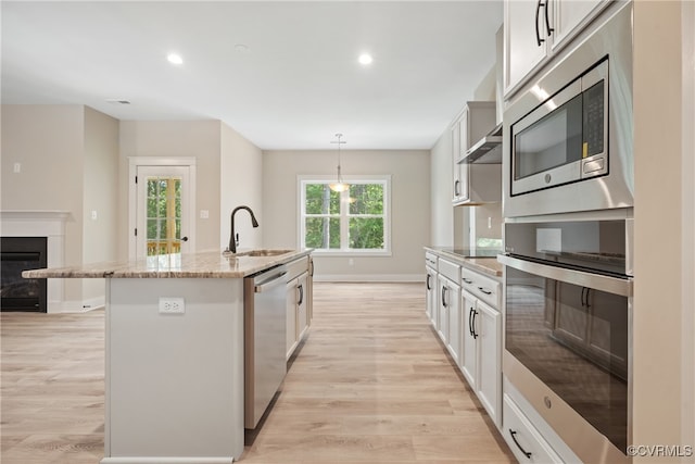 kitchen featuring white cabinetry, sink, appliances with stainless steel finishes, an island with sink, and light wood-type flooring