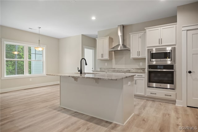 kitchen with white cabinetry, wall chimney range hood, sink, and an island with sink