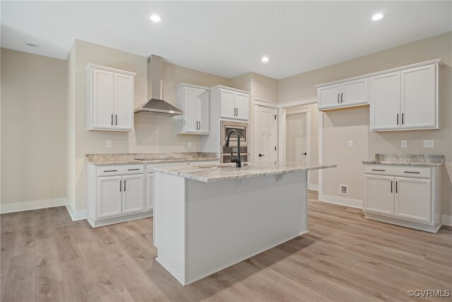 kitchen featuring light hardwood / wood-style floors, wall chimney exhaust hood, white cabinetry, and a kitchen island with sink