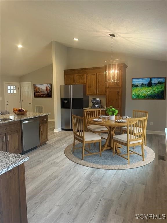 dining room with light hardwood / wood-style floors, a notable chandelier, and vaulted ceiling