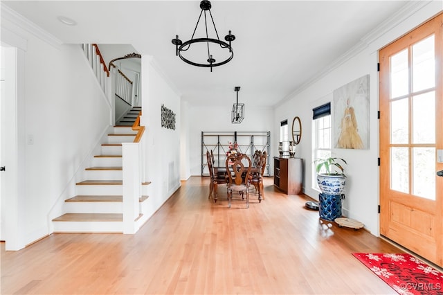 foyer entrance featuring light wood-type flooring, plenty of natural light, a notable chandelier, and crown molding