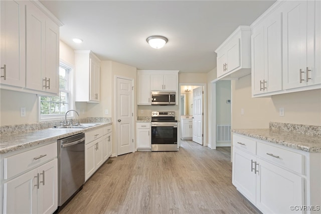 kitchen featuring light stone counters, white cabinets, light hardwood / wood-style flooring, sink, and appliances with stainless steel finishes