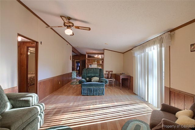 living room featuring ornamental molding, a textured ceiling, ceiling fan, light hardwood / wood-style flooring, and wood walls