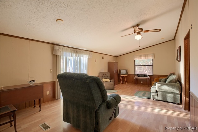 living room featuring a textured ceiling, ornamental molding, vaulted ceiling, and light wood-type flooring