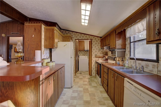 kitchen featuring white appliances, sink, washer / dryer, lofted ceiling, and wood walls