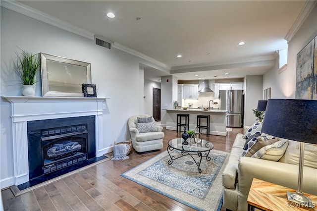 living room featuring sink, wood-type flooring, and ornamental molding