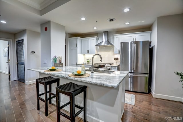 kitchen featuring a center island with sink, wall chimney exhaust hood, white cabinets, stainless steel fridge, and dark hardwood / wood-style flooring