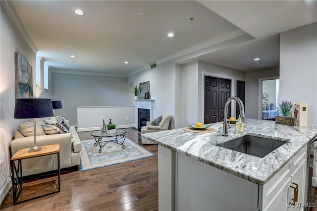 kitchen with light stone counters, hardwood / wood-style flooring, sink, ornamental molding, and white cabinetry