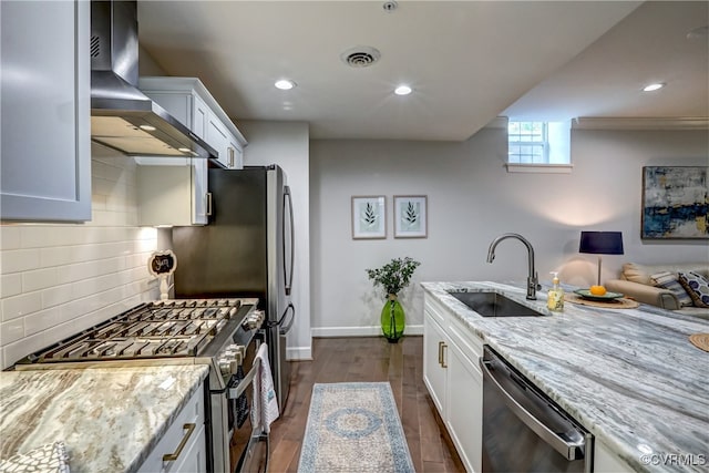 kitchen featuring white cabinets, stainless steel appliances, light stone counters, and wall chimney range hood