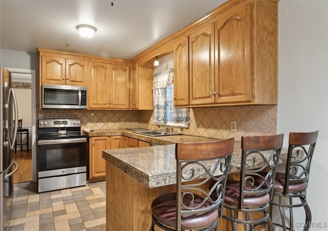 kitchen featuring kitchen peninsula, appliances with stainless steel finishes, backsplash, a kitchen breakfast bar, and sink